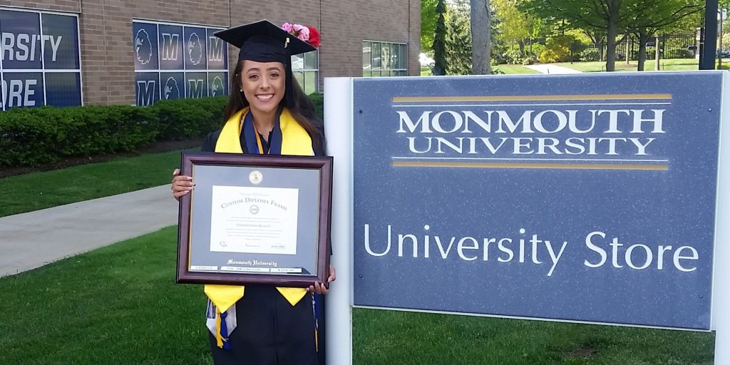 graduate wearing regalia standing outside holding a custom diploma frame