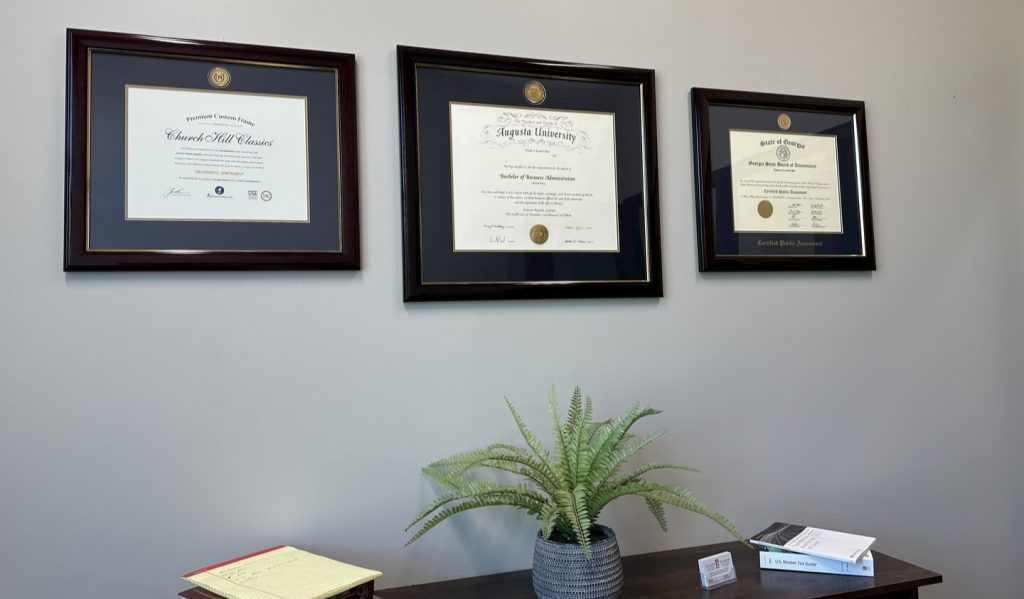 three custom diploma frames hung on office wall above desk and plant