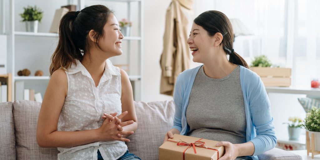 two female college roommates smiling at each other holding gift