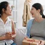 two female college roommates smiling at each other holding gift