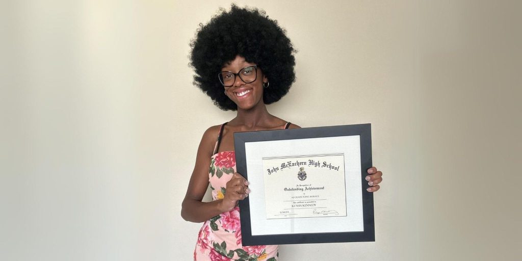 female graduate in dress smiling holding custom diploma frame