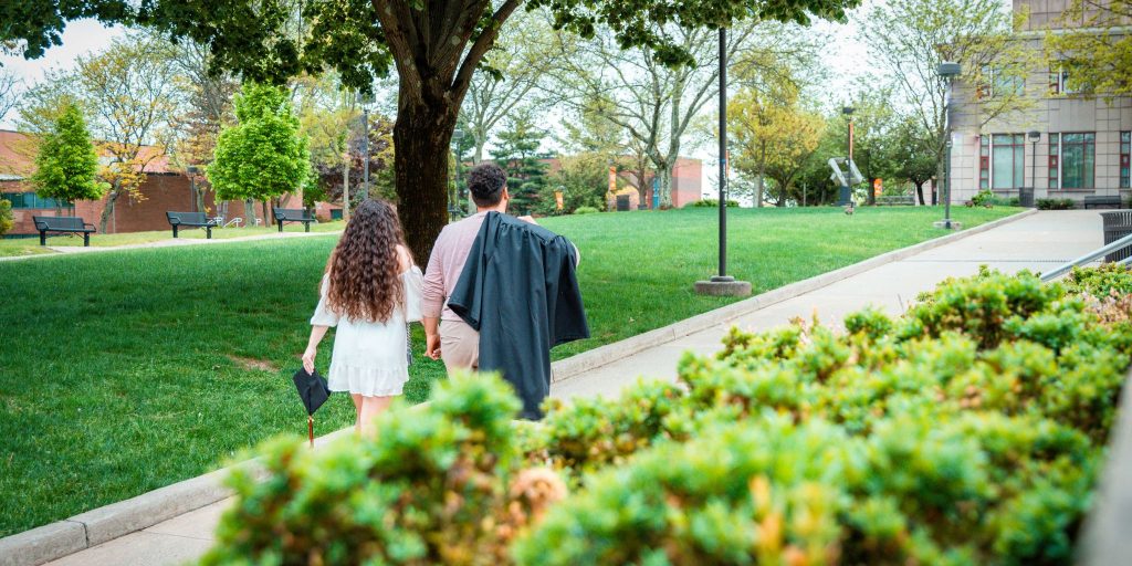 two graduates walking away from commencement holding regalia