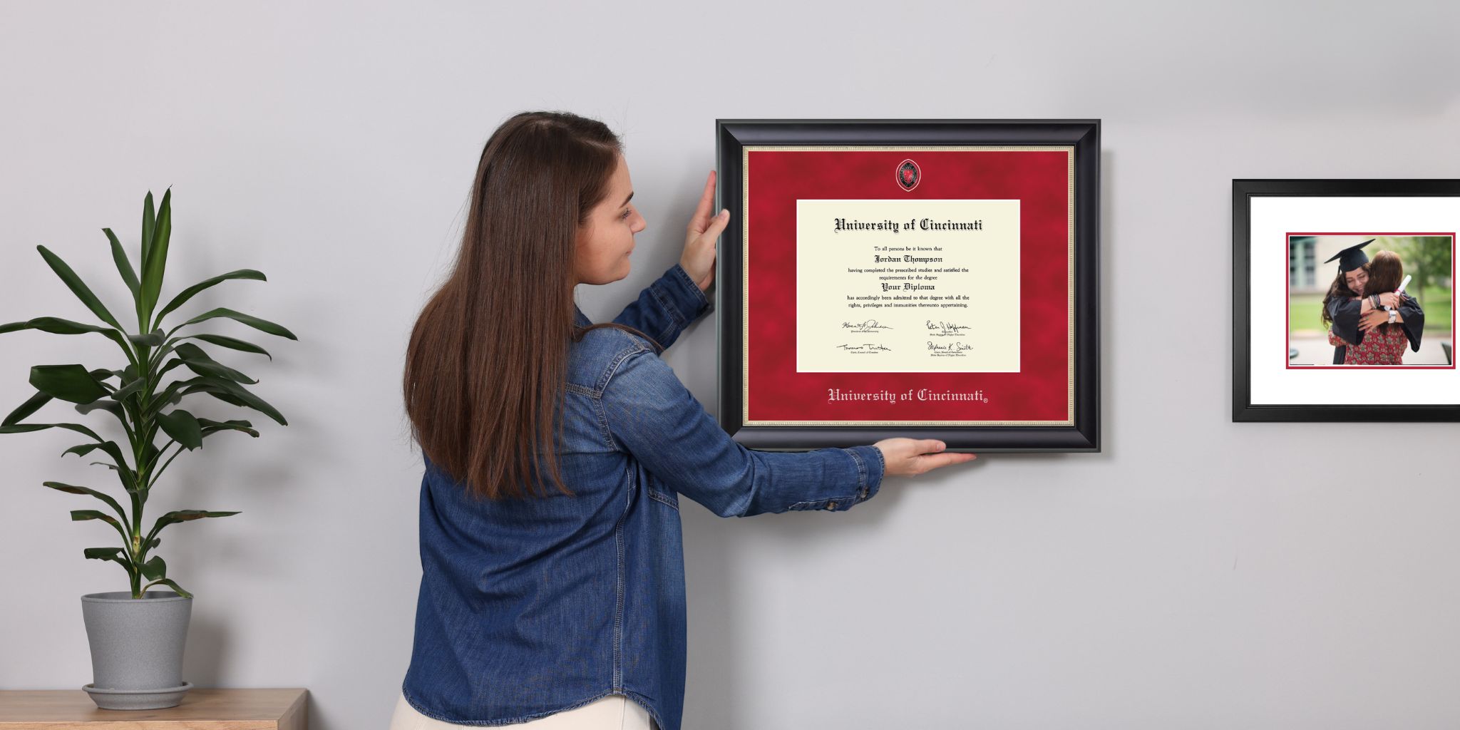 woman janging a custom diploma frame on wall next to plant and custom photo frame