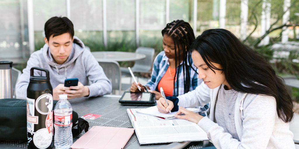 three college students sitting around an outdoor table studying