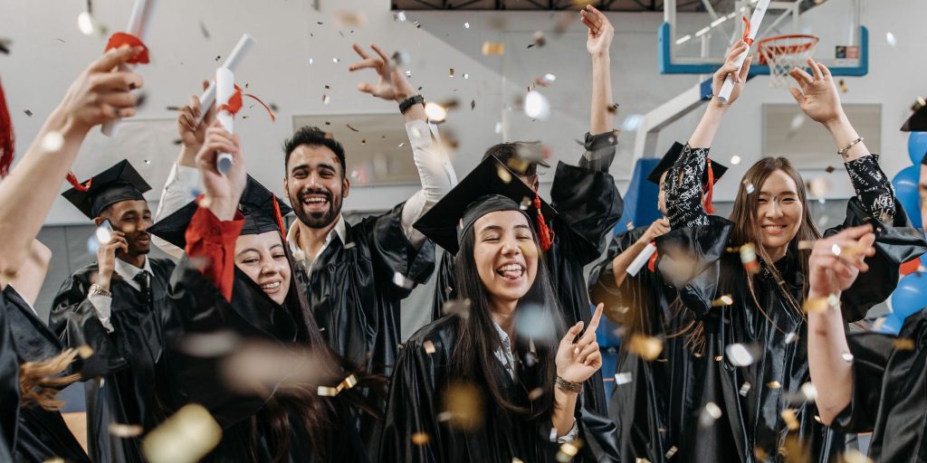 group of graduates celebrating and cheering in gymnasium with confetti