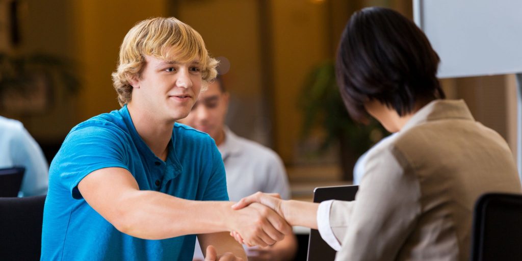 male college student in blue shirt shaking persons hand