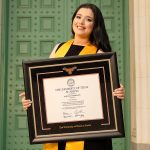 Smiling graduate in regalia holding a custom UT Austin diploma frame