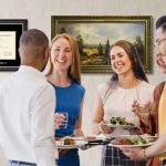 group of people mingling over food in front of wall with vanderbilt diploma frame