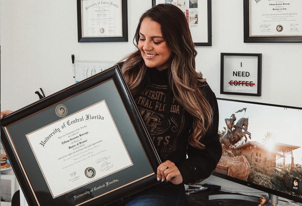 graduate in front of gallery wall holding university of central florida diploma frame