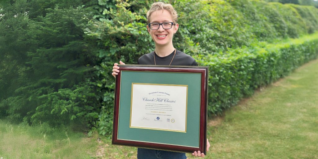 Smiling man holding a custom Church Hill Classics diploma frame outside in front of greenery
