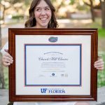 Smiling graduate holding a custom University of Florida diploma frame outside