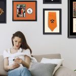 Woman on couch with Princeton diploma frame, 2025 photo frame and grad regalia frames behind her on wall.