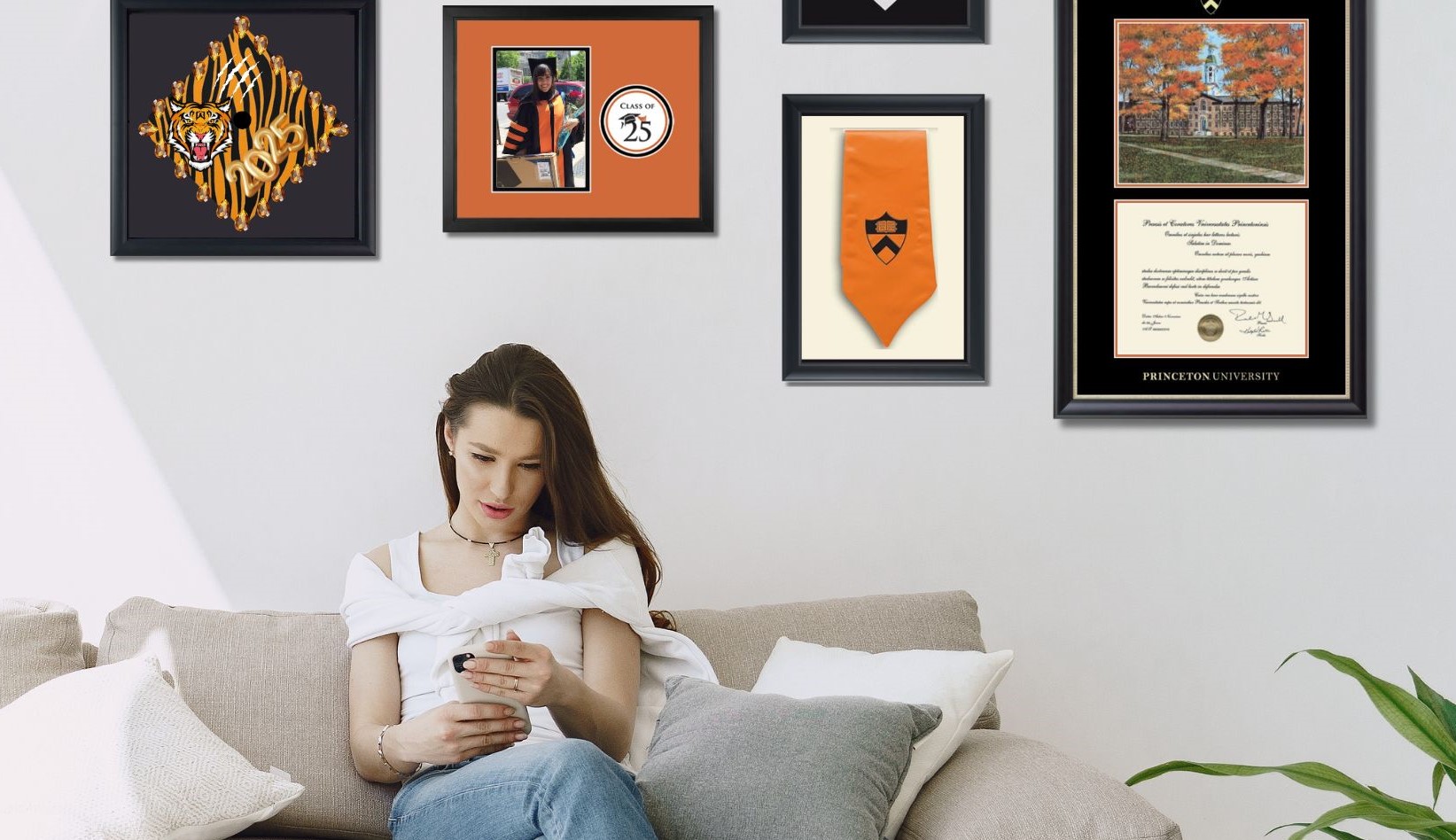 Woman on couch with Princeton diploma frame, 2025 photo frame and grad regalia frames behind her on wall.