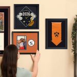 college student hanging custom photo frame on gallery wall featuring grad cap shadow box frame, graduation stole frame, and Princeton University campus scene diploma frame