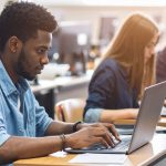 College students working on laptops in busy campus classroom.