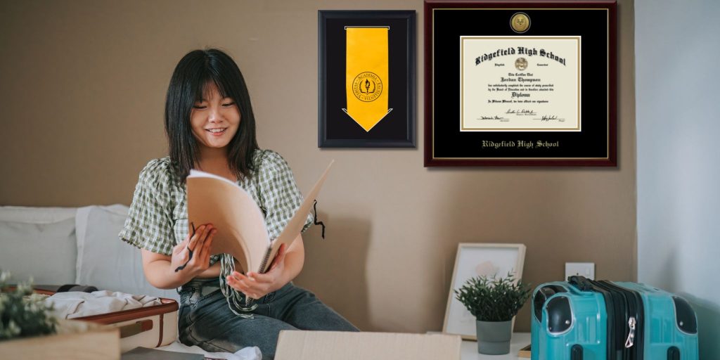high school grad looking at folder with stole frame and high school diploma frame on wall behind them