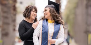 mom smiling at her daughter wearing mortarboard and blue graduation stole