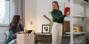 two girls in a dorm room decorating walls with a custom photo frame on desk