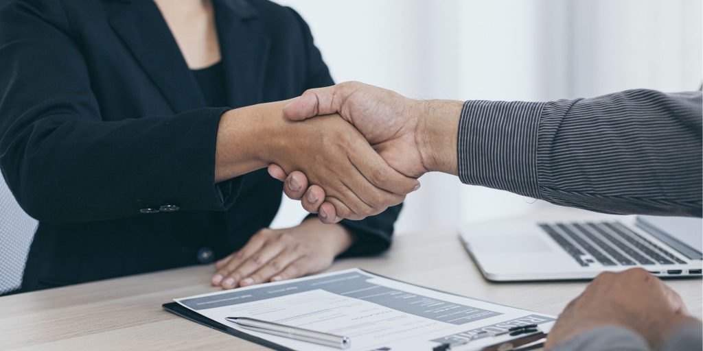 closeup of handshake between interviewee and interviewer over resume on desk