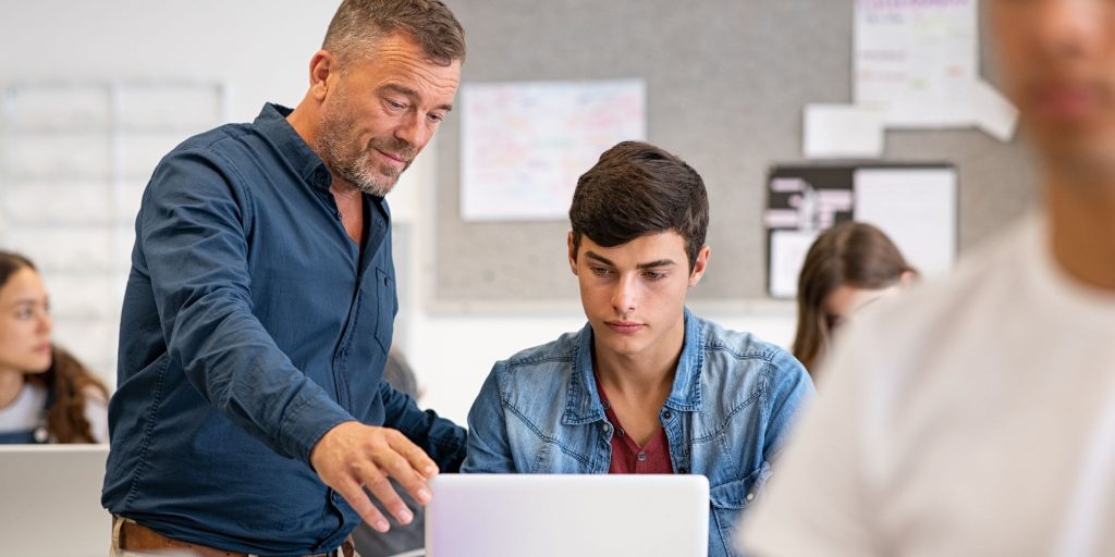 professor in classroom helping student working on computer