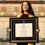 Smiling graduate holding a custom University of Texas Austin diploma frame