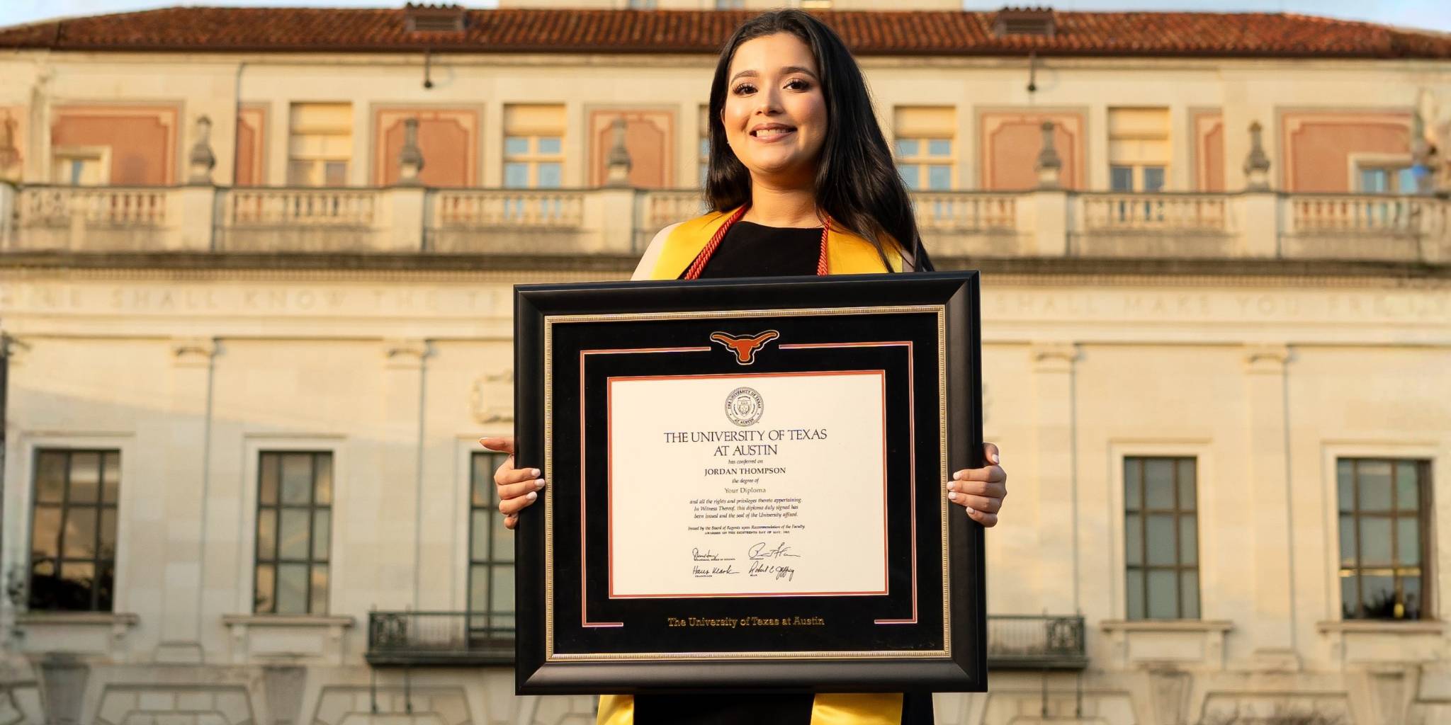 Smiling graduate holding a custom University of Texas Austin diploma frame