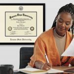 woman working at a desk with custom plaque and diploma frame on wall behind her