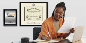 woman working at a desk with custom plaque and diploma frame on wall behind her