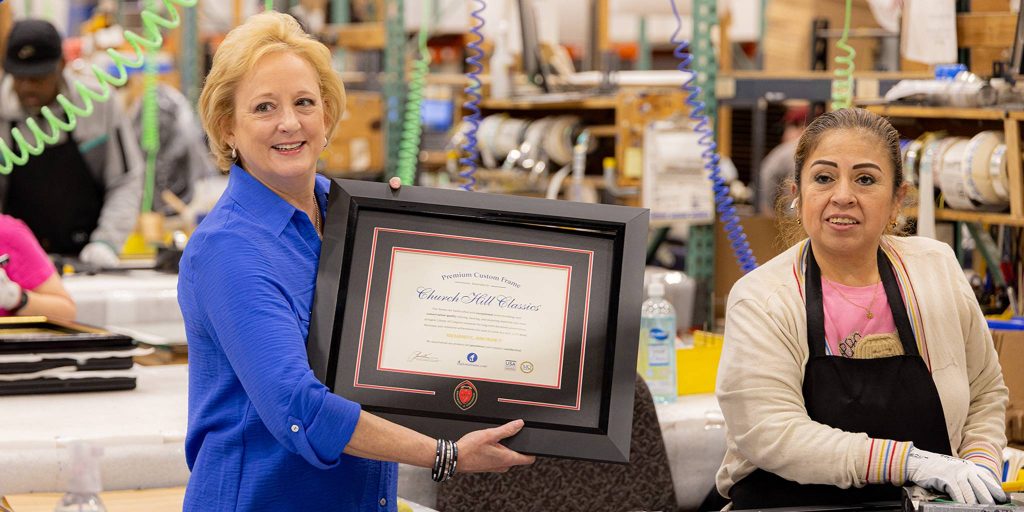 Lucie Voves on Church Hill Classics production floor with smiling employee holding custom diploma frame