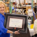 Lucie Voves on Church Hill Classics production floor with smiling employee holding custom diploma frame