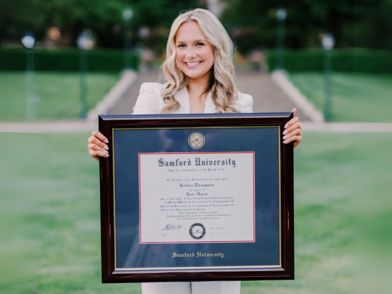a smiling graduate holding a custom Samford University diploma frame from Church Hill Classics
