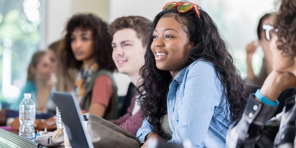 Closeup of students sitting in college class with laptops on table.