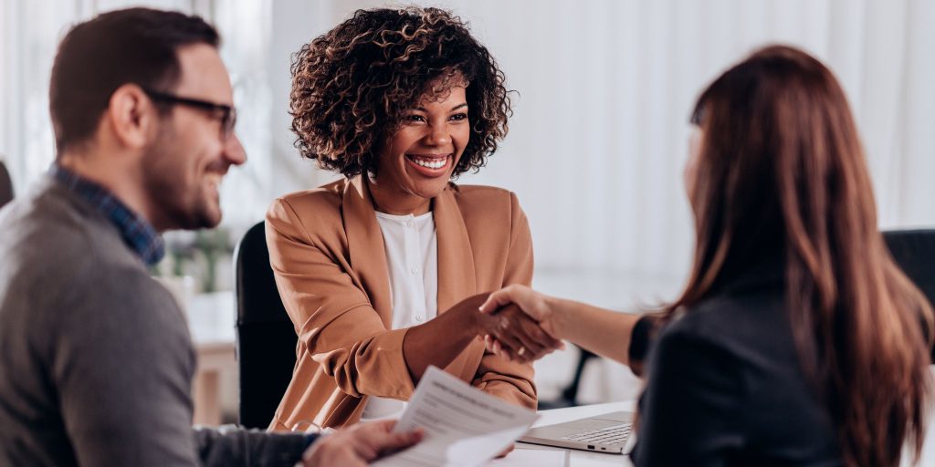 smiling woman shaking hands with interviewer as man with resume looks on.