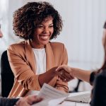 smiling woman shaking hands with interviewer as man with resume looks on.