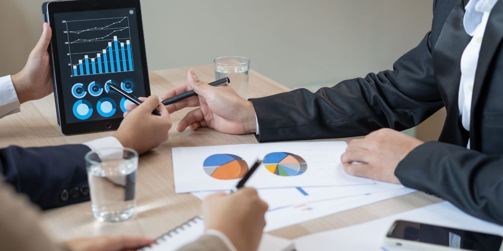 Closeup of hands pointing to bar graphs on tablet at business desk.