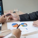 Closeup of hands pointing to bar graphs on tablet at business desk.
