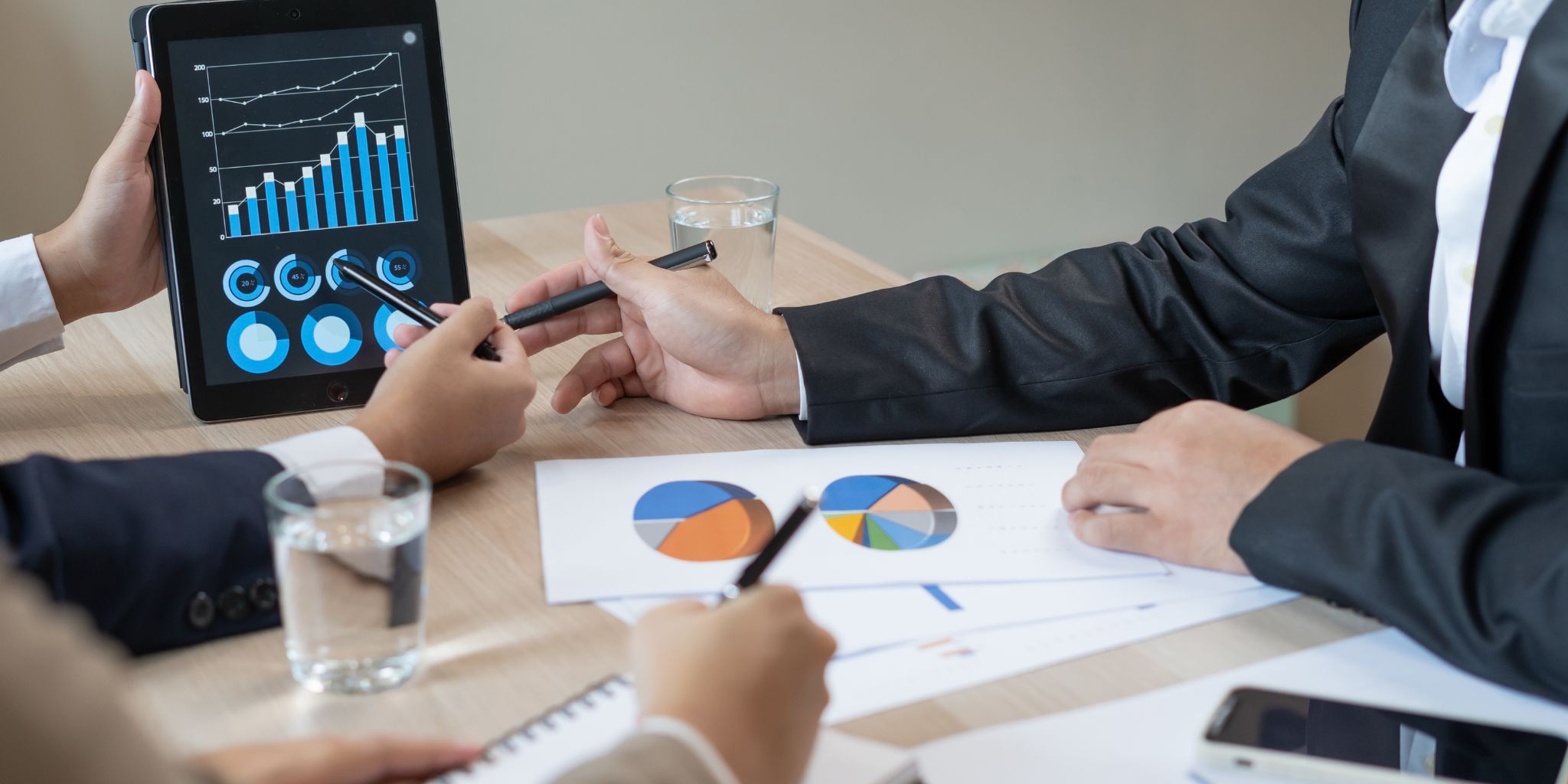 Closeup of hands pointing to bar graphs on tablet at business desk.