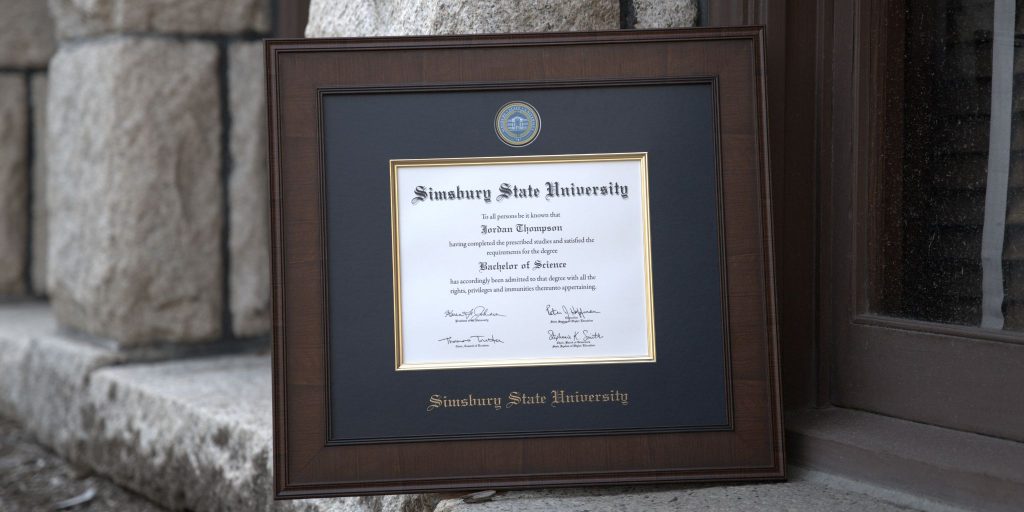 Simsbury State University diploma frame leaning against stone bulding.