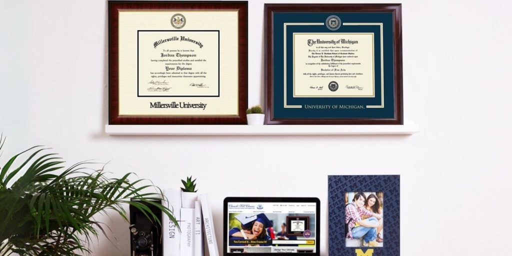 Millersville University and University of Michigan diploma frames on shelf above desk with laptop and UMichigan photo frame on it.