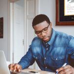 Man working at desk with Boston University diploma frame on wall behind him.