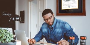 Man working at desk with Boston University diploma frame on wall behind him.