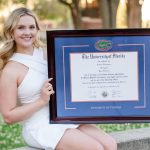 Smiling university of florida graduate holding a custom UF spirit diploma frame