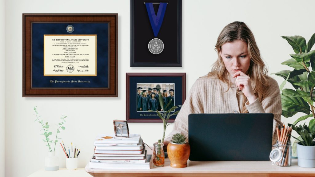 Woman on laptop at desk with Penn State diploma frame and medallion frame on wall behind her.