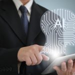 Closeup of man in suit holding laptop with AI graphic hovering above it.