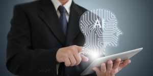 Closeup of man in suit holding laptop with AI graphic hovering above it.
