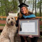woman smiling outside next to her dog holding a custom UNI diploma frame