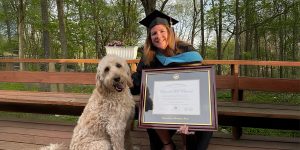 woman smiling outside next to her dog holding a custom UNI diploma frame