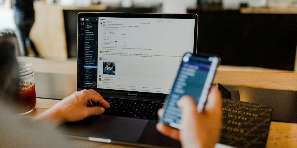 Closeup of a laptop with a person's hand on the keyboard and the other hand holding a cell phone.