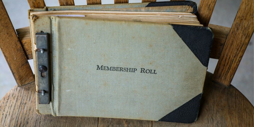 Closeup of a vintage book on a chair that says "Membership Roll" in capital letters on front of cover.