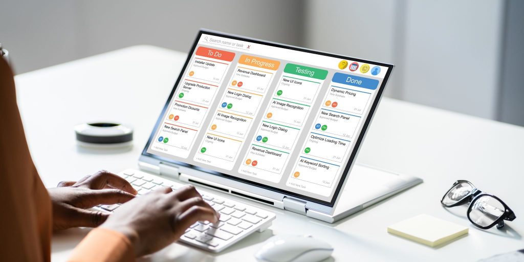 Closeup of hands typing on a computer at a desk in an office with a digital scheduling calendar onscreen.